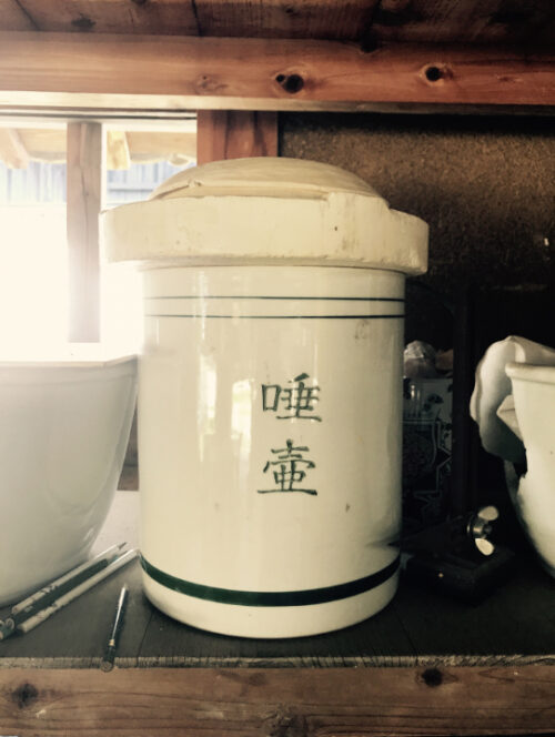 痰壺の写真。棚に乗った白い壺。「唾壺」と書かれている。